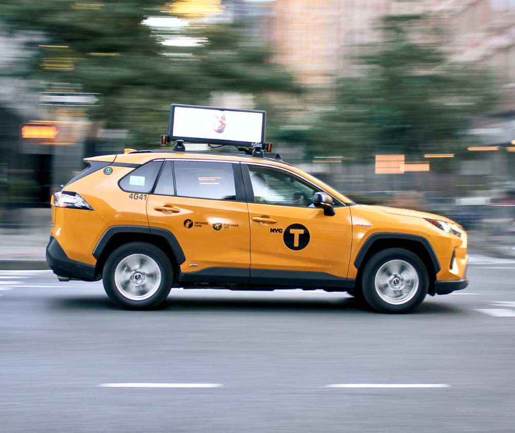 Picture of taxi driving with a digital ad sign on top of the car